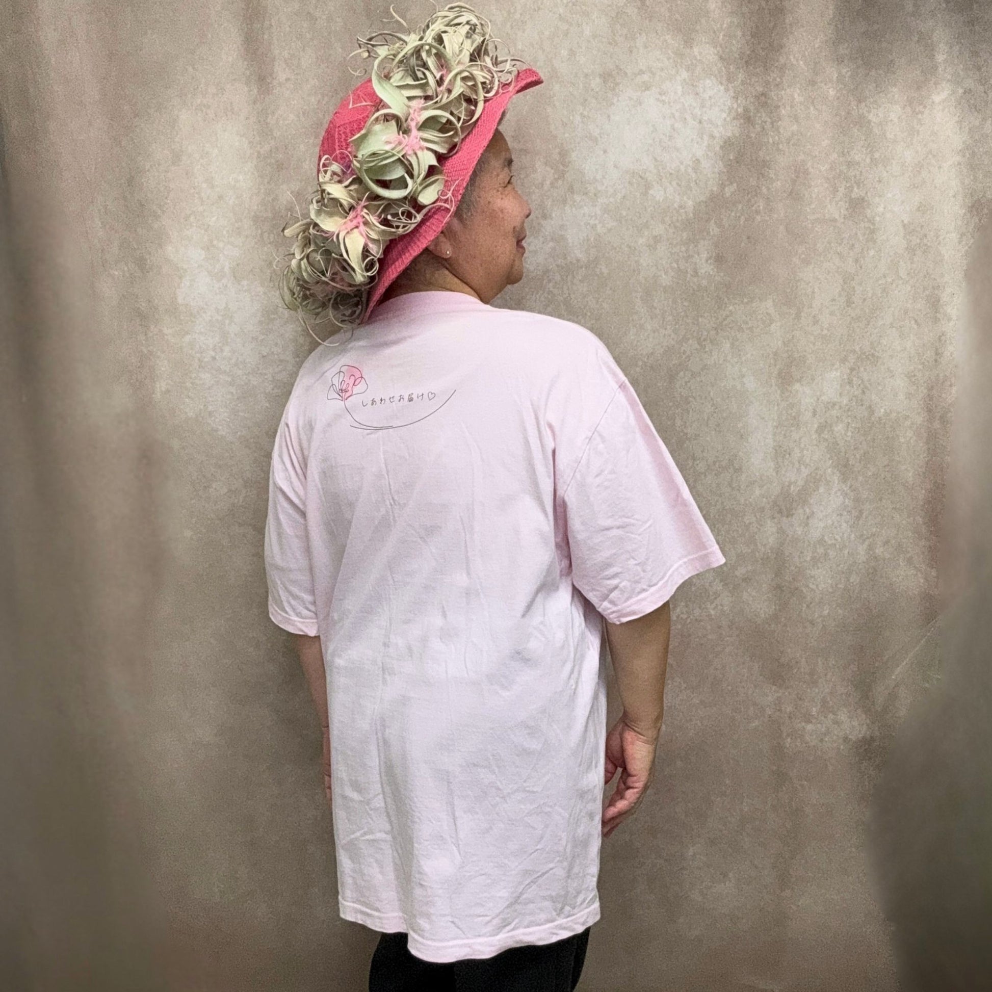 しあわせお届けTシャツ半袖の着用例で、オゼジュン先生がXXLサイズを後ろから着用した全身画像、背面プリントとゆったりした着用感がわかるやわらかなピンク色のTシャツ、花創人ガーデニング教室